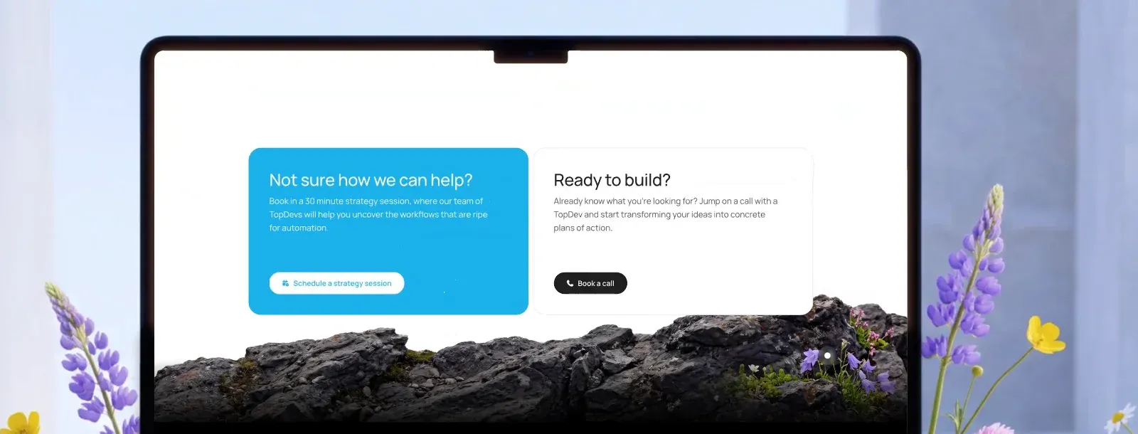 A laptop showing the Topdevs call to action cards above a dark rock ridge with lupines and campanula